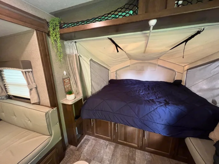 Cozy RV rental: Pop-up bed with blue comforter, sofa, and hanging plant decor create a comfy camper interior.. Forest River Rockwood Roo 2019