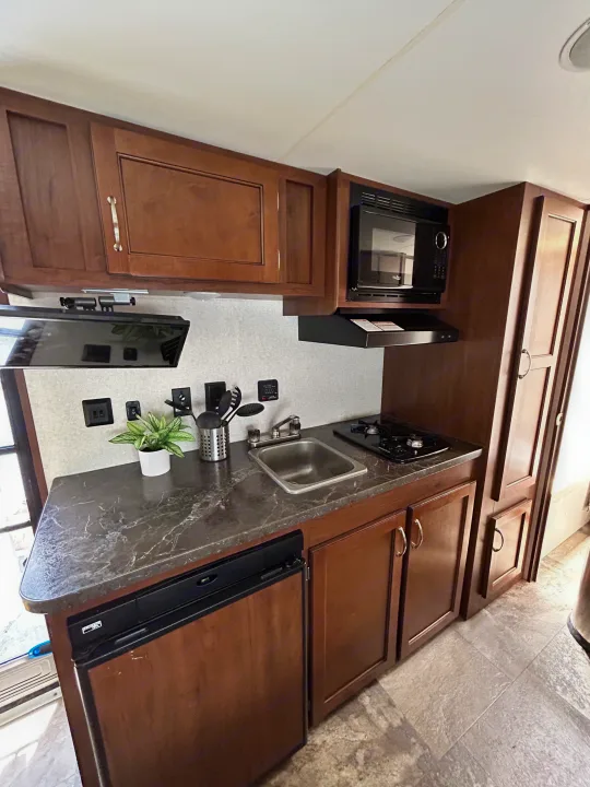 Compact RV rental kitchen with wood cabinets, dark countertop, sink, stove, microwave, and fridge, perfect for travel.. Jayco Jay Flight SLX 2017