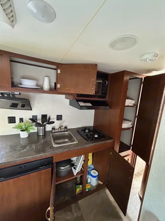 Inside an RV rental: a well-equipped compact kitchen with sink, stovetop, microwave, fridge, and storage.. Jayco Jay Flight SLX 2017