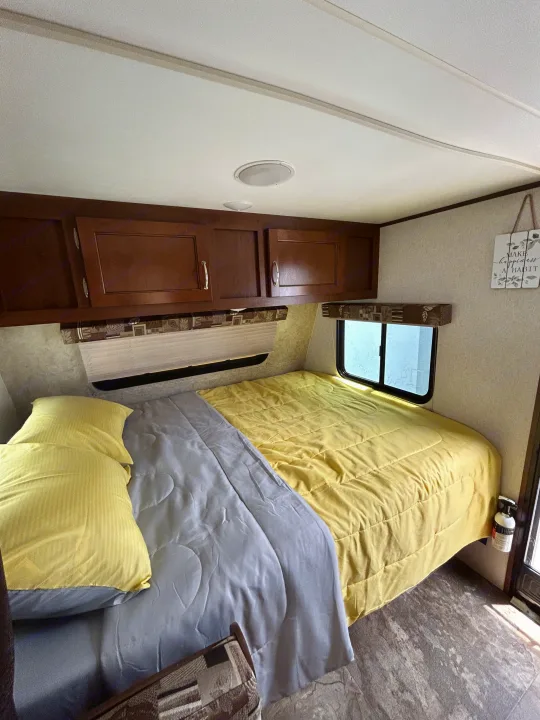 Bright RV rental bedroom with a bed, yellow comforter, overhead storage, and window. Includes a fire extinguisher.. Jayco Jay Flight SLX 2017