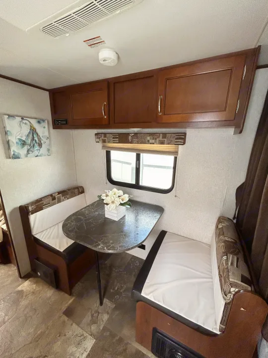 RV rental dinette setup with cushioned benches, a marblized table, and wooden overhead cabinets, perfect for travel.. Jayco Jay Flight SLX 2017