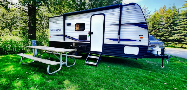 An inviting Springdale rv rental travel trailer set up at a green campsite with a picnic table.. Keystone RV Springdale 2022