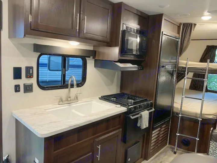 RV rental interior: A compact kitchen with sink, stove, microwave, fridge, and bunk beds visible. Ready for your travels!. Jayco Jay Flight SLX 2019