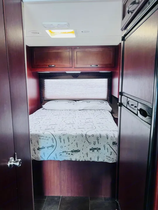 RV rental interior: Cozy bedroom with camping-themed bedding, overhead storage, and fridge access.. Thor Freedom Elite 2015