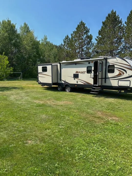 Spacious RV rental set up in a lush grassy field, surrounded by trees under a clear sky. Ideal for outdoor adventures.. Keystone RV Bullet Ultra Lite 2015