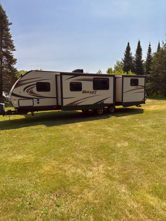 Travel trailer RV rental, a Bullet Ultra-Lite by Keystone, set up on a grassy field under a clear blue sky.. Keystone RV Bullet Ultra Lite 2015