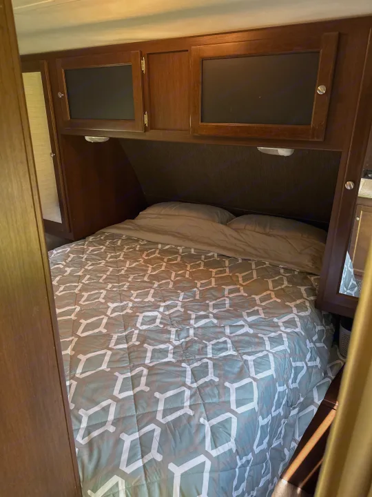 RV rental bedroom with bed, patterned comforter, pillows, and wooden overhead cabinets with built-in lights.. Keystone RV Bullet Ultra Lite 2015