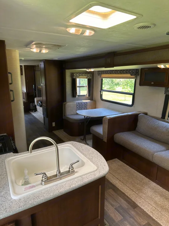 An RV rental's inviting interior with a kitchen sink, dinette booth, and sofa, showcasing ample living space.. Keystone RV Bullet Ultra Lite 2015