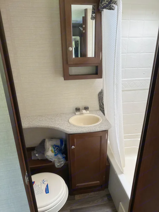 This compact RV rental bathroom features a sink, wood vanity, mirror, toilet, and shower/tub combo.. Keystone RV Bullet Ultra Lite 2015