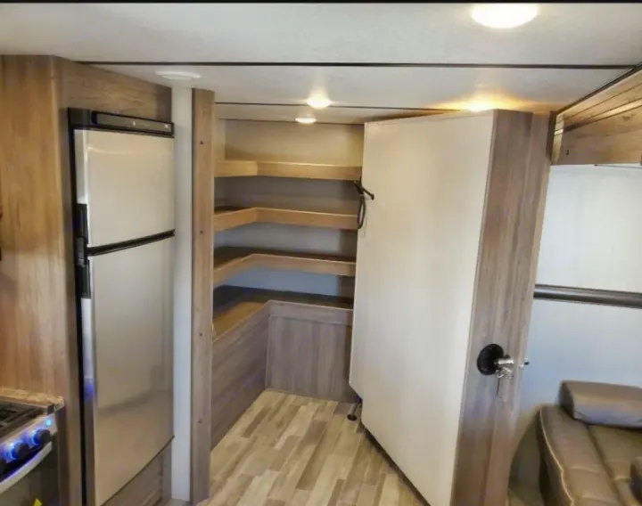 Spacious RV rental interior featuring a full-size refrigerator, corner pantry shelves, and a cozy living area sofa.. Crossroads RV Zinger 2020