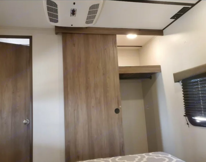 Explore this RV rental's bedroom, featuring a wood-grain sliding barn door, integrated closet, and overhead AC.. Crossroads RV Zinger 2020