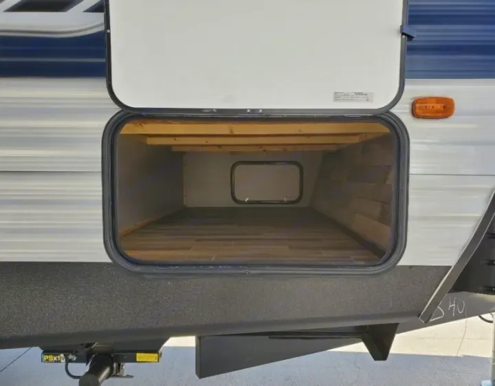 This RV rental features a spacious exterior storage compartment, open to show its clean wooden interior, ideal for travel trailer gear.. Crossroads RV Zinger 2020