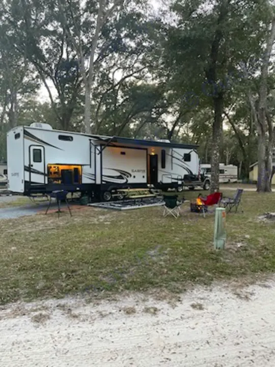 Enjoy a cozy evening at your RV rental campsite! This spacious RV is set up with a campfire, chairs, and picnic area under tall trees.. Forest River Sabre 2022