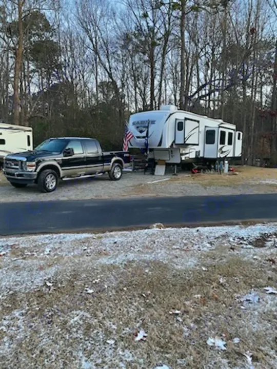A large white fifth-wheel RV is parked with a pickup truck at a snowy campsite, showcasing an ideal rv rental setup.. Forest River Sabre 2022