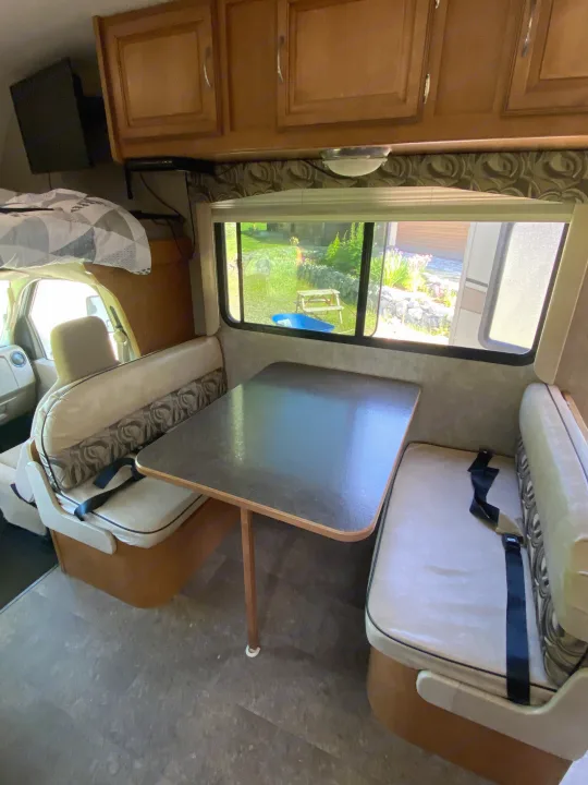 Inside an RV rental: Dinette with seatbelts, overhead cabinets, and comfy bunk. Ready for the road!. Winnebago Minnie Winnie 2015
