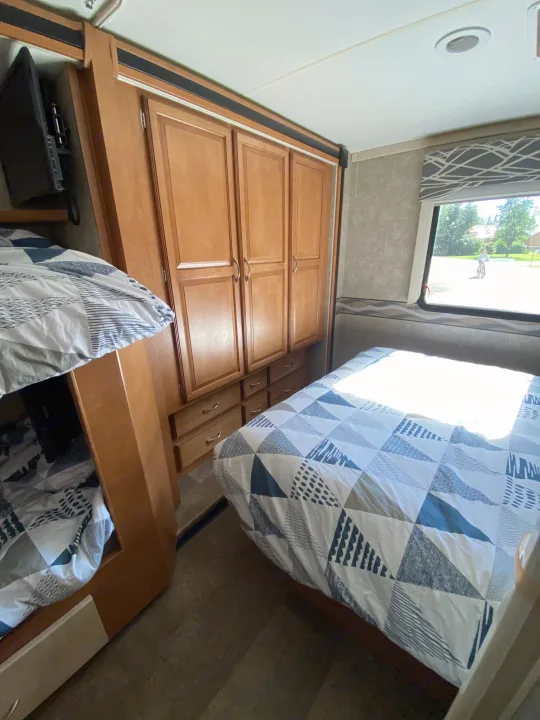 RV rental bedroom: main bed with geometric bedding, bunk beds, wood cabinets, and window view with a person on a bike.. Winnebago Minnie Winnie 2015