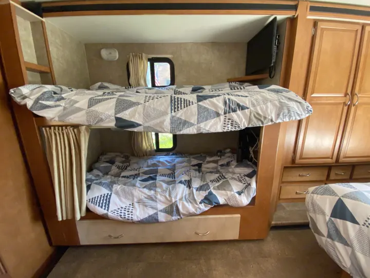 Inside an RV rental: two bunk beds with patterned bedding, a TV on top bunk, and storage. Ideal family sleeping.. Winnebago Minnie Winnie 2015
