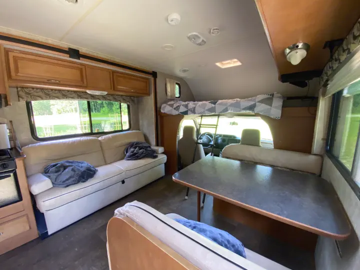Bright RV rental interior showcasing a living area with a sofa, dining table, and overhead bed.. Winnebago Minnie Winnie 2015