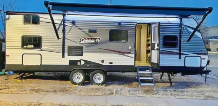 This Coleman travel trailer, an excellent RV rental option, is set up with its door open and awning extended.. Dutchmen Coleman Lantern 2019