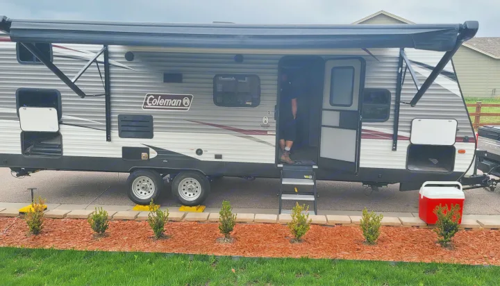 This travel trailer RV rental is set up for adventure: awning extended, steps down, wheels on blocks. Cooler nearby.. Dutchmen Coleman Lantern 2019