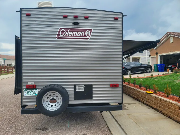 The rear of a grey Coleman travel trailer, possibly an RV rental, with a spare tire, parked on a paved driveway.. Dutchmen Coleman Lantern 2019