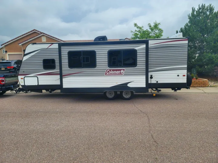Large Coleman travel trailer, possibly an RV rental, parked on asphalt in front of a house on a cloudy day.. Dutchmen Coleman Lantern 2019