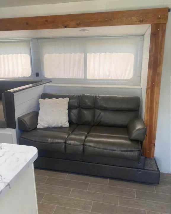 Modern RV rental living space: cozy dark sofa, bright windows with shades, and rustic wood beam accents.. Forest River Cherokee Grey Wolf 2021