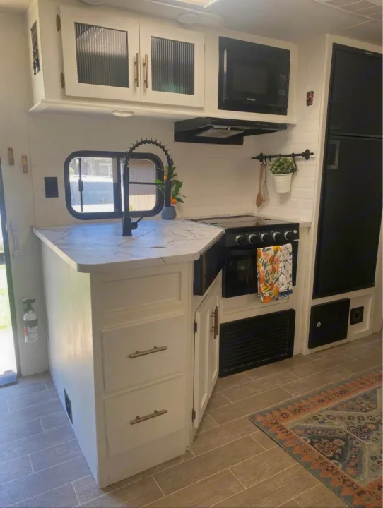Step inside this modern RV rental kitchen. Features white cabinets, black appliances, marble-look counters, & subway tile backsplash.. Forest River Cherokee Grey Wolf 2021