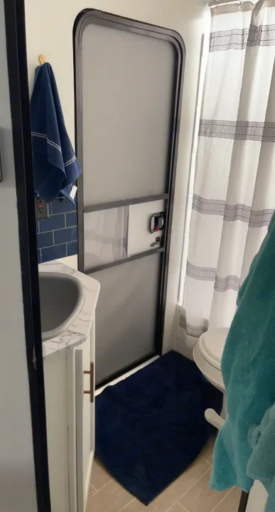 This RV rental's compact bathroom features a vanity with sink, blue tiled backsplash, shower, toilet, and an interior RV door.. Forest River Cherokee Grey Wolf 2021