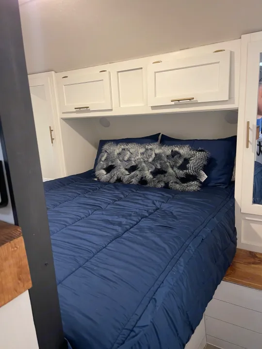 Cozy RV rental bedroom with navy blue bedding, a faux fur pillow, and practical overhead storage cabinets.. Forest River Cherokee Grey Wolf 2021