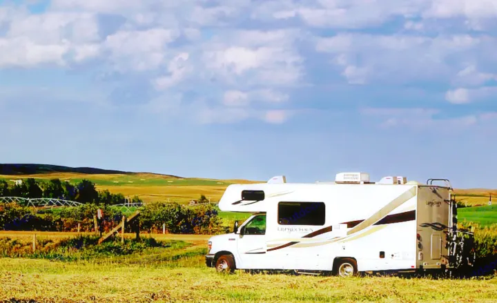 White RV rental with bikes on back, parked in a golden field, under a cloudy blue sky with distant rolling hills.. Forest River Coachmen Leprechaun 2014