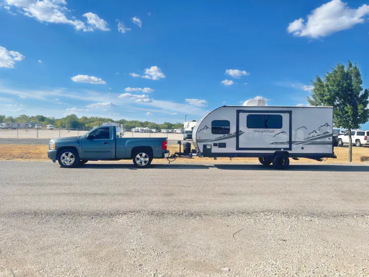 A teal pickup truck tows a grey Wolf Pup travel trailer, ready for an RV rental adventure on a clear day.. Forest River Cherokee Wolf Pup Black Label 2022