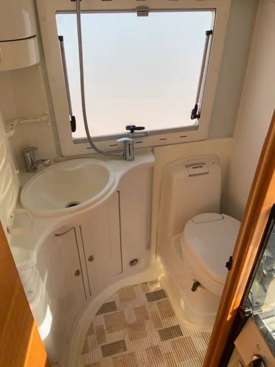Inside an RV rental bathroom, featuring a compact sink with shower attachment, toilet, and window.. Fiat Ducato 2005