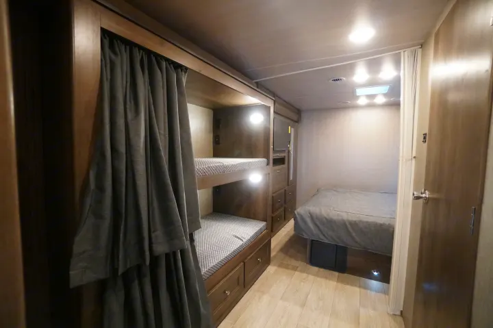 Inside this modern rv rental: cozy bunk beds with curtains, a comfortable main bed, and storage cabinetry.. Nexus Triumph 32T 2023