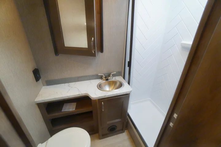 RV rental bathroom: compact vanity, sink, mirrored cabinet, and modern shower with white herringbone walls.. Nexus Triumph 32T 2023