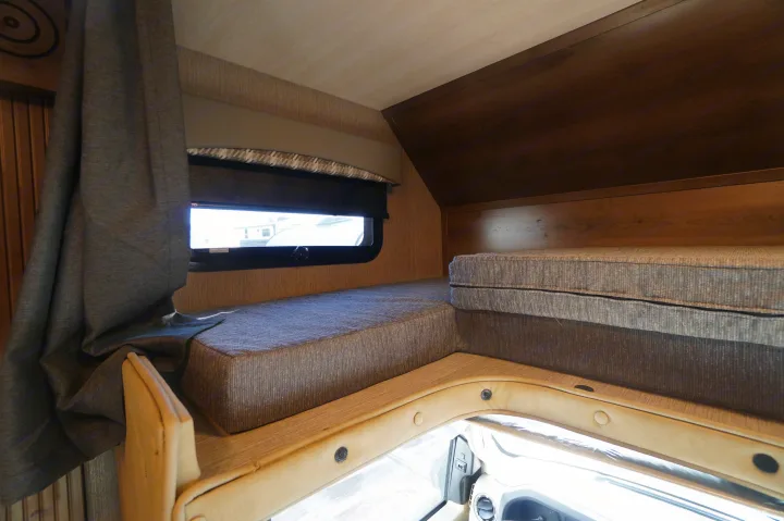 This RV rental interior features cozy bunk beds with gray cushions, a window with a blind, and a drawn privacy curtain.. Nexus Triumph 32T 2023