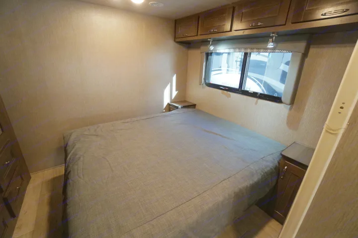 Inside an rv rental, a bedroom with a neatly made bed, overhead cabinets, and a window for views. Includes bedside tables.. Nexus Triumph 32T 2023