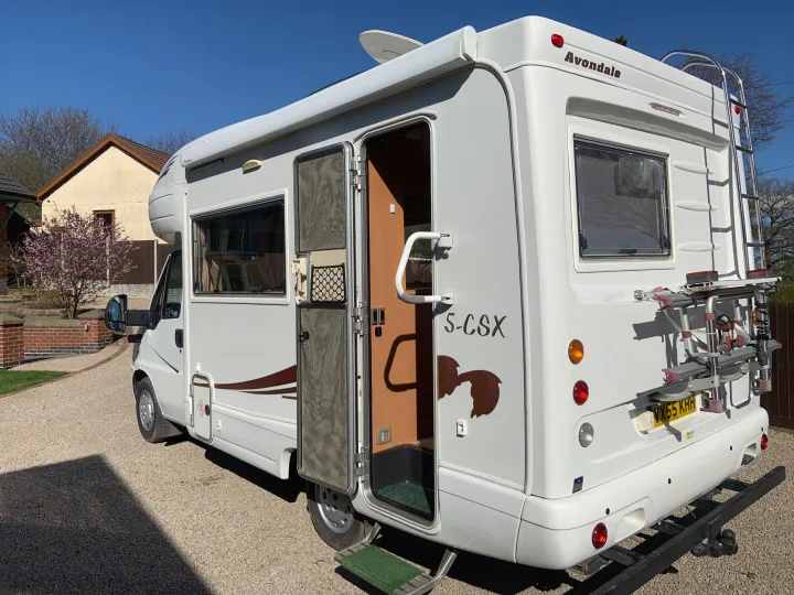 A white Avondale motorhome, a common rv rental choice, is parked on a gravel driveway with its side door open and a bike rack.. Fiat Ducato 2005