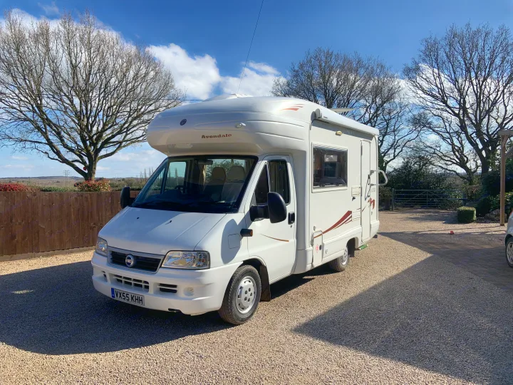 A white Avondale motorhome, ideal for an RV rental, parked on a sunny gravel driveway surrounded by bare trees under a blue sky.. Fiat Ducato 2005