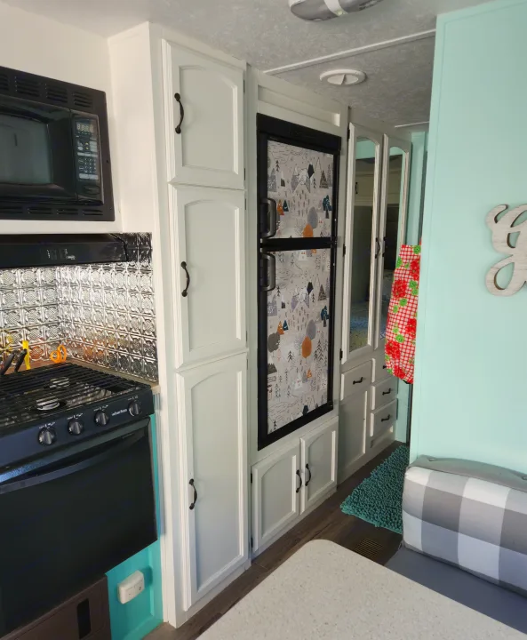 Renovated RV rental kitchen area features white cabinets, a black microwave, and a refrigerator with a mountain pattern.. Forest River Palomino Puma 2009