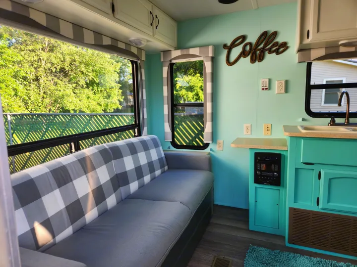 Bright rv rental interior featuring a cozy plaid sofa, light blue walls, coffee sign, and a compact kitchenette.. Forest River Palomino Puma 2009