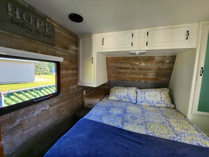 RV rental bedroom: wood walls, comfy bed, white cabinets, window view, & 'Hope Anchors the Soul' sign.. Forest River Palomino Puma 2009