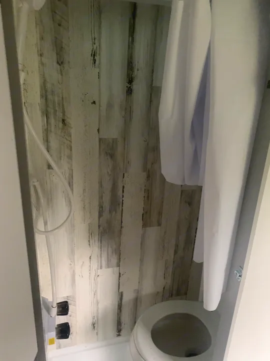 RV rental: Compact wet bath with toilet, shower hose, and white curtain against rustic wood-look walls.. Travel Lite Rove 14BH 2024