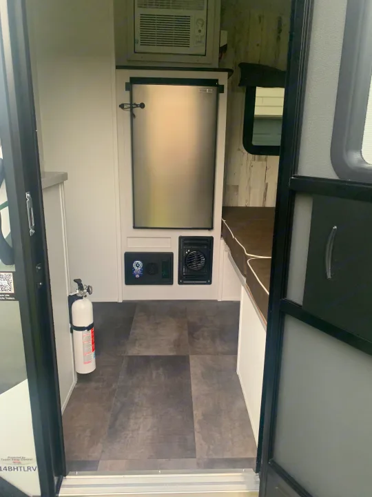 Compact RV rental interior with refrigerator, AC, and a fire extinguisher. Ideal for comfortable travel.. Travel Lite Rove 14BH 2024