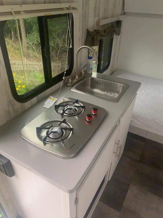 Bright RV rental interior featuring a compact kitchen with a sink, Suburban stove, and cozy sleeping area.. Travel Lite Rove 14BH 2024