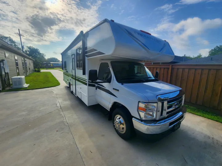 White Class C Freelander RV rental parked on a concrete driveway. Residential setting with fence & sky.. Coachmen Freelander 2023
