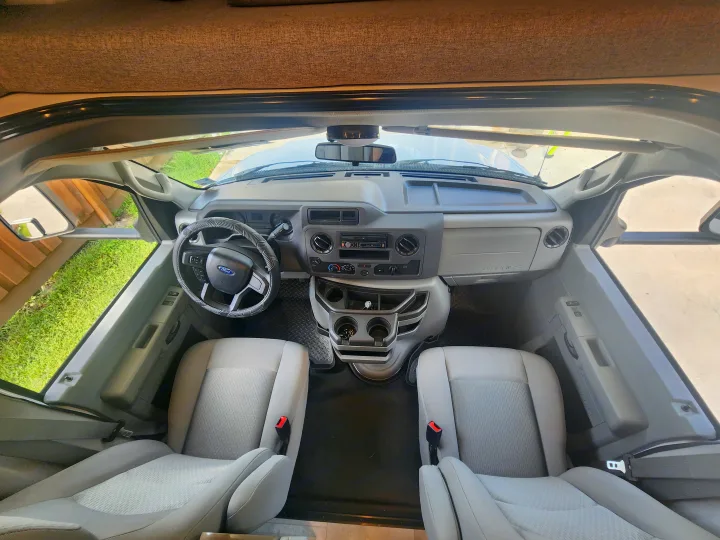 Overhead view of an RV rental cockpit showcasing the dashboard, steering wheel, and front seats.. Coachmen Freelander 2023