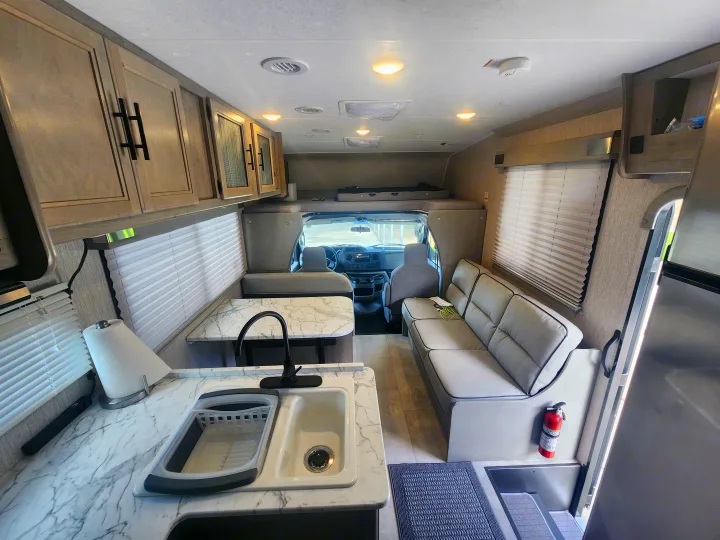 Spacious RV rental interior with modern kitchen, marble-look counter, sink, comfortable dinette seating, and essential fire extinguisher.. Coachmen Freelander 2023
