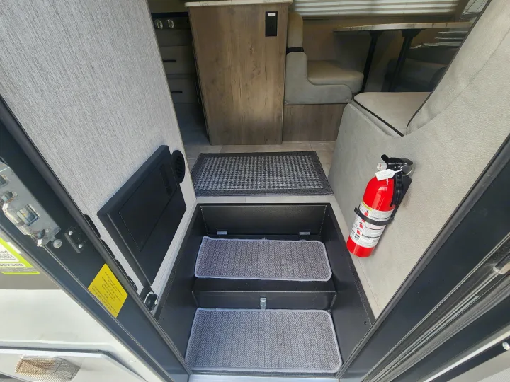 This RV rental interior features carpeted steps, a mounted fire extinguisher, and a cozy dining area, ready for your adventure.. Coachmen Freelander 2023