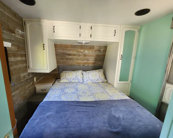 Cozy RV rental bedroom with a comfortable bed, wood accent wall, and practical overhead storage cabinets.. Forest River Palomino Puma 2009